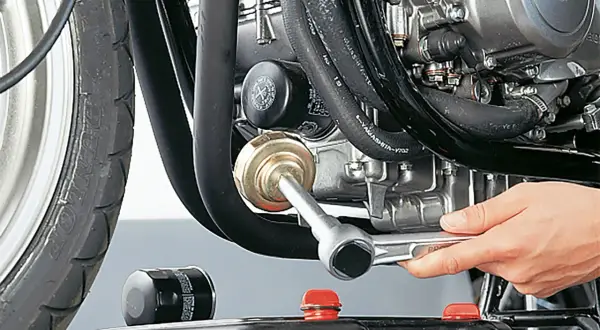 Motorrad-Ölfilter wird mit einem Werkzeug gewechselt, daneben ein neuer Filter und eine Ölauffangwanne.