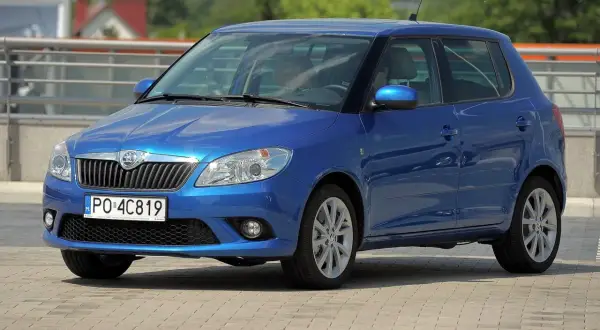 Niebieska Skoda Fabia 2, z nowymi żarówkami w reflektorach, parkuje na placu.