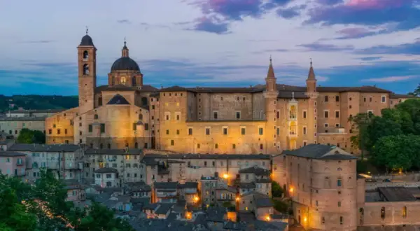 Urbino Natale: il Palazzo Ducale illuminato al crepuscolo, con le sue torri e la cupola, domina la città storica.