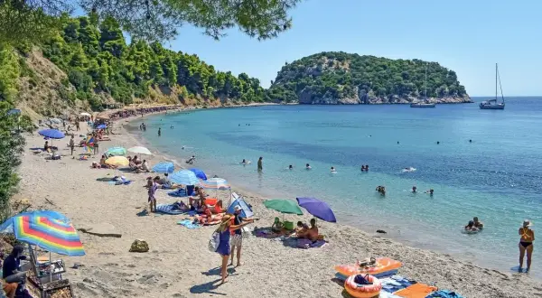 Słoneczny dzień na plaży w Chalkidiki. Ludzie opalają się, pływają w turkusowej wodzie, a kolorowe parasole rzucają cień.