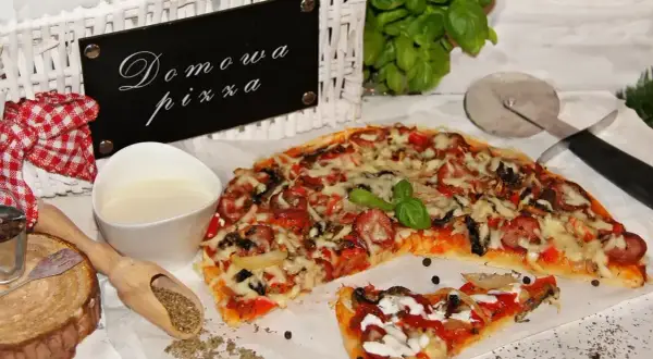Domowa pizza bez drożdży, z kiełbasą i warzywami, gotowa do podania. Obok sos i przyprawy.
