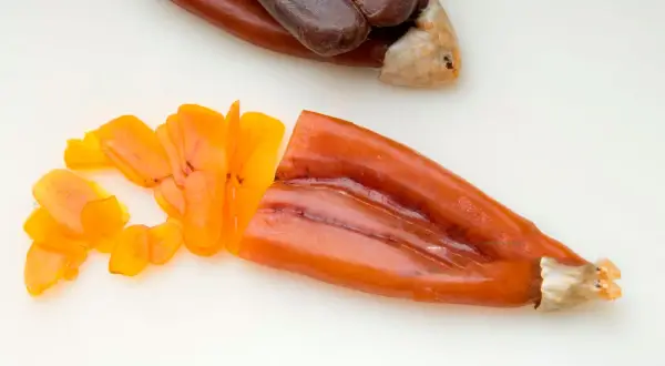 Bottarga en español: huevas de pescado curadas, una entera oscura y otra naranja cortada en láminas finas.