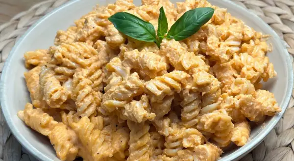 Fusilli conditi con una cremosa salsa al pesto e pomodorini, guarniti con foglie di basilico fresco.