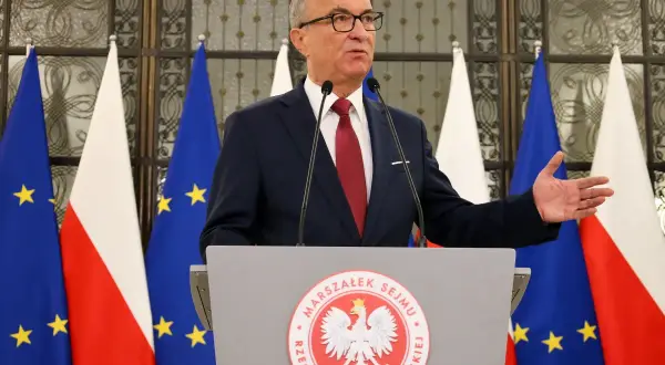 Marszałek Sejmu przemawia na tle flag Polski i UE, gestykulując. Mowa dotyczy odrzucenia weta prezydenta.