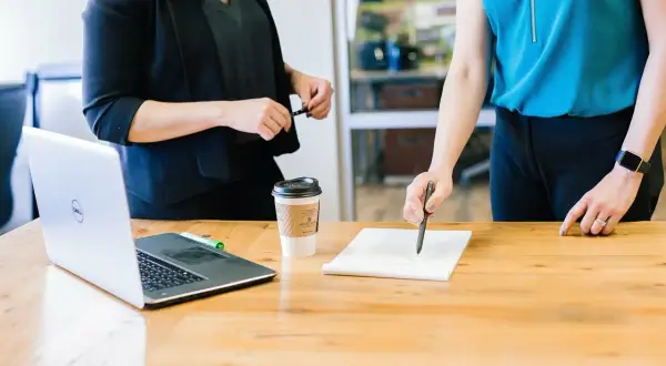 Dwie kobiety omawiają umowę ramową przy biurku z laptopem i kawą.