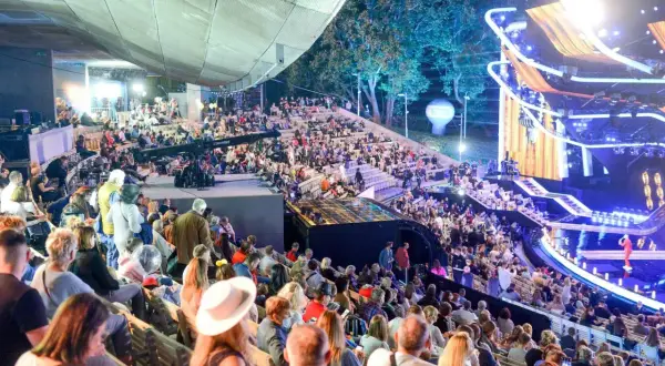 Tłumy widzów na amfiteatralnych trybunach podczas festiwalu w Opolu. Na scenie widowiskowe oświetlenie i dekoracje.