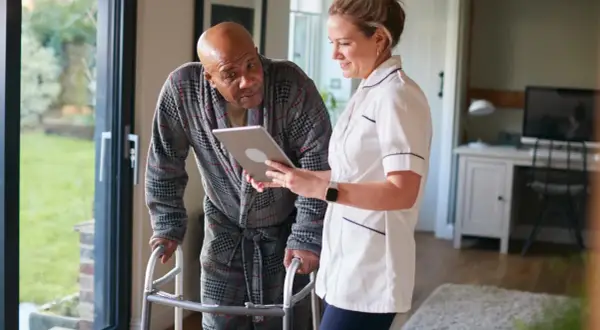 Pflegekraft zeigt Mann mit Gehhilfe auf Tablet, wie oft kann man eine Reha beantragen.