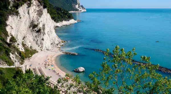 Spiaggia dei frati con scogliere bianche, mare azzurro e alberi verdi.