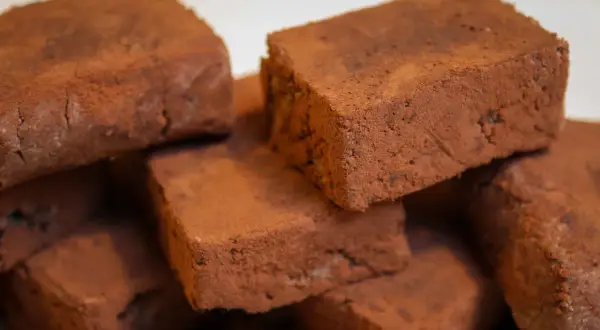 Stapel von schokoladigen Rohkost-Brownies, bestäubt mit Kakaopulver. Ein gesunder Genuss!