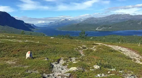 Vacker vy över en sjö och berg, med en stenröse markerad med rött. En vandringsled leder mot horisonten, kanske på väg mellan Kvikkjokk och Saltoluokta.