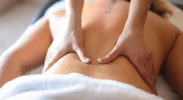 Mains expertes prodiguant un massage corporelle relaxant sur un dos, enveloppé dans une serviette douce.