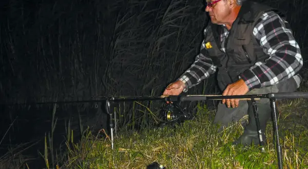 Ein Angler mit Stirnlampe prüft nachts seine John Sidley Rig-Ausrüstung am Ufer.