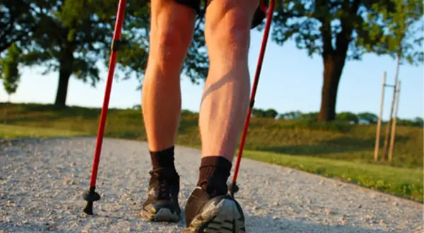Nogi w butach i skarpetach, z kijkami nordic walking. Dowiedz się, jak prawidłowo założyć buciki na kijki nordic walking, by cieszyć się spacerem.