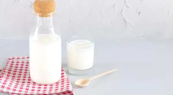 Bouteille de lait et verre sur une serviette à carreaux. Le lait battu, c'est quoi ? C'est ce lait frais et crémeux.