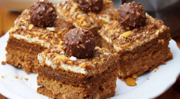 Pyszne ciasto Ferrero Rocher z kremem i orzechami, udekorowane całymi czekoladkami.