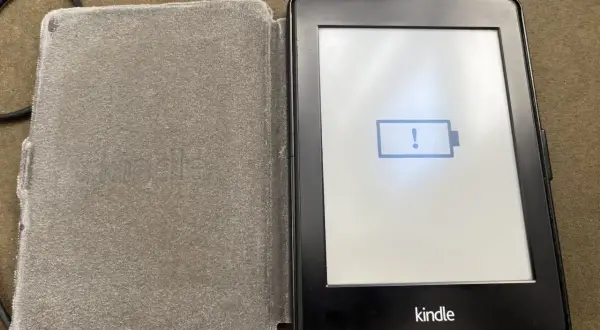 Un Kindle avec une batterie faible, prêt à être éteint. L'icône de batterie vide et le point d'exclamation indiquent qu'il est temps de le charger.