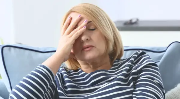 Kobieta z dłońmi na czole, zamyślona, zastanawia się, czy miastenia jest uleczalna.