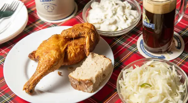 Knusprige Henne Berlin mit Brot, Krautsalat und einem Bierkrug.