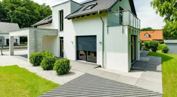 Nowoczesna, biała elewacja domu z panelami słonecznymi na dachu, przeszklonym balkonem i minimalistycznym ogrodem.