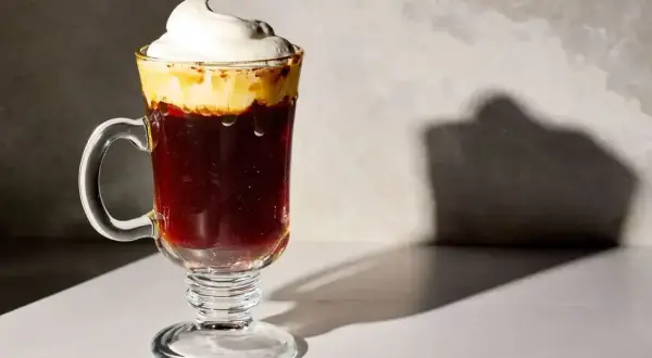 En härlig kaffedrink med vispad grädde som toppar den mörka drycken i ett glas med fot.
