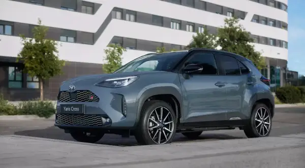 Szary Toyota Yaris Cross benzyna z czarnymi akcentami stoi przed nowoczesnym budynkiem.