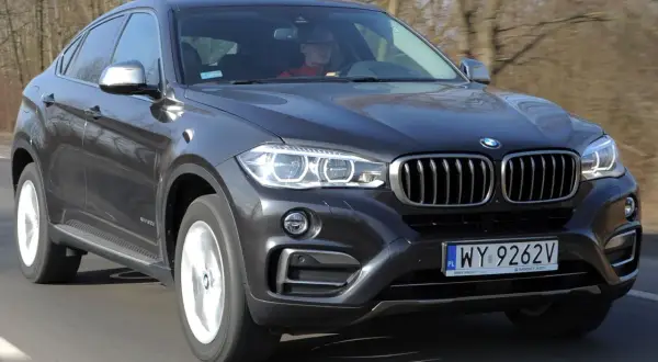 Ciemnoszary BMW F16 z kierowcą za kierownicą jedzie po drodze.