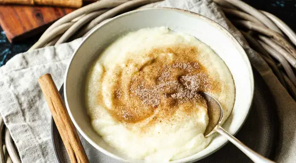 Cremiger Grießbrei mit Zimt und Zucker bestreut, ein einfaches und leckeres Grießbrei Rezept. Daneben liegen Zimtstangen.