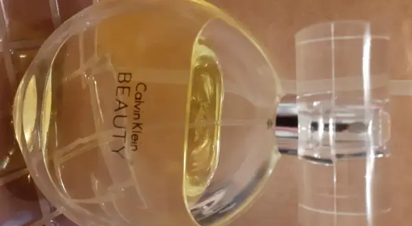 Flakon perfum Calvin Klein Beauty 100 ml, o bursztynowym kolorze, stoi na brązowym tle.