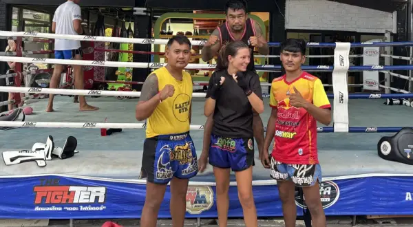 Fyra personer poserar i en ring för c4 thaiboxning. En kvinna i mitten med tränare på var sin sida.
