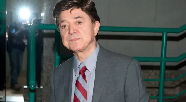 Jerzy Połomski w szarym garniturze i krawacie, otoczony przez błyski fleszy.
