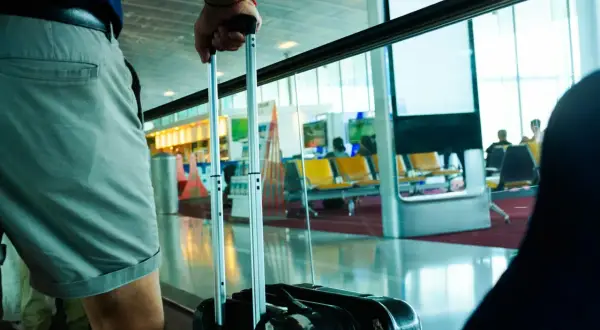 Osoba z wizzair bagażem czeka na lotnisku. W tle widać poczekalnię z żółtymi siedzeniami.