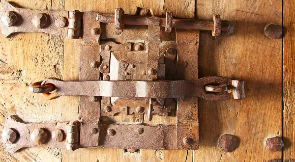 Parti di una serratura antica in ferro battuto su una porta di legno. I meccanismi arrugginiti suggeriscono una lunga storia.