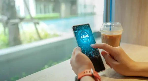 Dłoń trzyma smartfon z ikoną eSIM na ekranie, obok napoju.