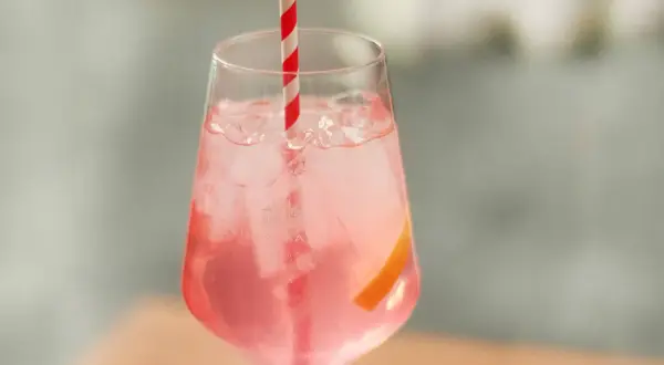 Erfrischender Sarti Spritz mit Eiswürfeln, einer Orangenscheibe und einem rot-weißen Strohhalm.