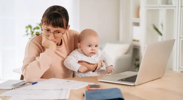 Mère pensive avec bébé, jonglant entre le travail et le renouvellement congé parental CAF.