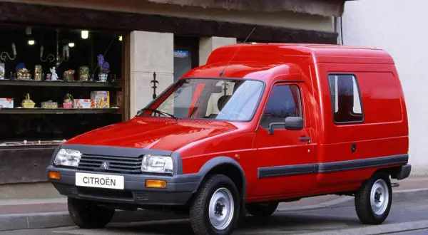 Czerwony Citroen C15, dostawczy klasyk, parkuje przed sklepem z upominkami.