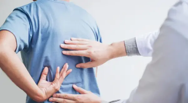 Dłoń terapeuty bada plecy pacjenta, szukając oznak bólu. Może to być wstęp do terapii, ale warto pamiętać o potencjalnych skutkach ubocznych nastawiania kręgosłupa.