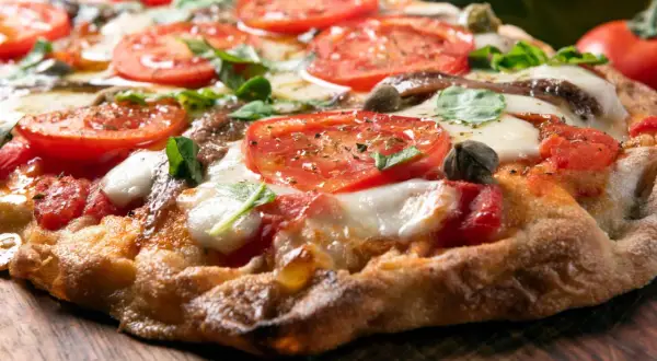 Knusprige Pizza mit Tomaten, Mozzarella und Basilikum auf einem Holzbrett.