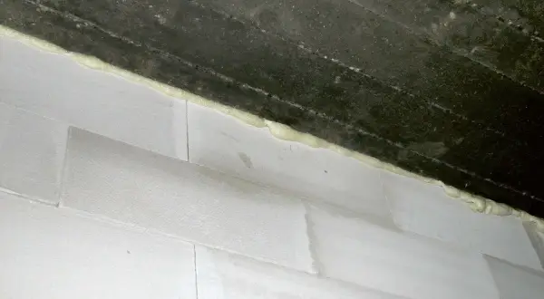 Dylatacja komina wykonana pianką montażową między betonowym stropem a białymi bloczkami.