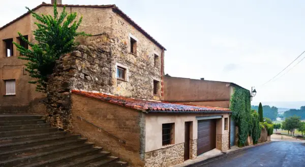Escaleras de piedra suben hacia casas tradicionales de piedra y estuco, con tejados de teja roja. Una enredadera cubre parte de una pared.