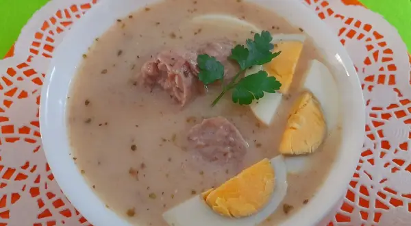 Pyszny żurek na rosole z kiełbasą i jajkiem, udekorowany natką pietruszki.