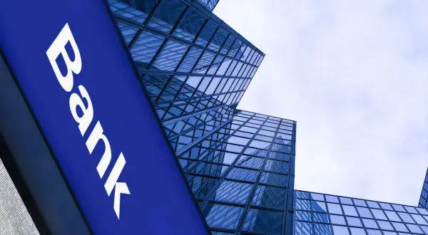 Niebieski szyld z napisem "Bank" na tle nowoczesnych, szklanych wieżowców. Czy to bank z 1600 roku?