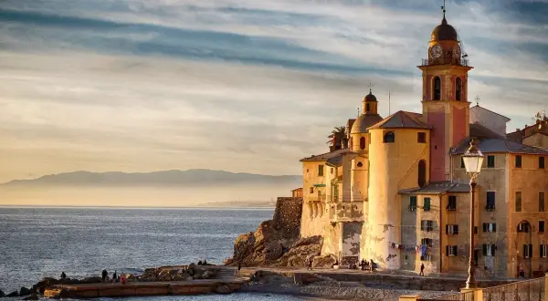 Solnedgång över Camogli, Italien. Kyrkan med sitt klocktorn lyser i kvällssolen vid havet.