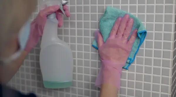 Ręce w różowych rękawiczkach czyszczą płytki. Zastanawiasz się, czym umyć fugi? Spray i ściereczka to dobry początek.