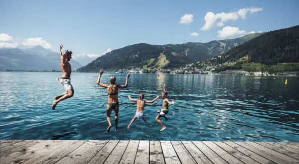 Familj hoppar i vattnet en solig zell am see sommar. Berg och stad i bakgrunden.