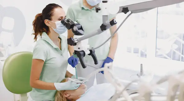 Dentystka z asystentką przy mikroskopie stomatologicznym, przygotowujące się do zabiegu, być może wyrywania ósemki.
