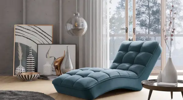 En lyxig, blå schäslong fåtölj med quiltad design står i ett modernt vardagsrum med konst och en stor fönsterdörr.