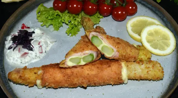 Knuspriges Spargel Cordon Bleu mit Schinken und Käse, serviert mit Dip, Tomaten und Zitrone.