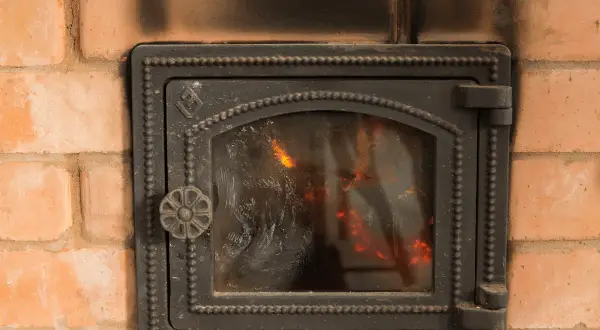 Porta del camino in ghisa annerita dal fumo, con fiamme visibili all'interno. Utile per capire come pulire il marmo del camino annerito.
