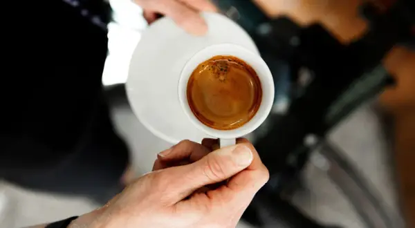 En hand håller en kopp med en perfekt dubbel espresso, med gyllene crema som lovar en intensiv smakupplevelse.